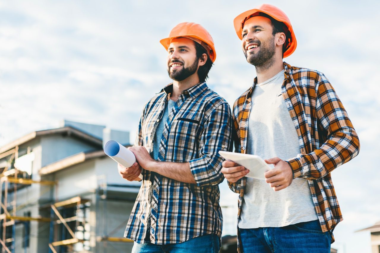 roofing contractor-with-blueprint-and-tablet-looking-away-at-construction-site